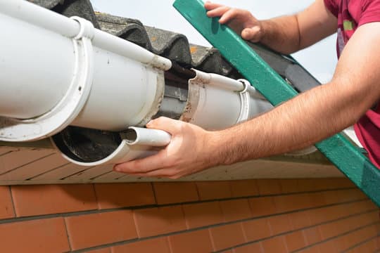 Technician performing gutter repairs on residential home